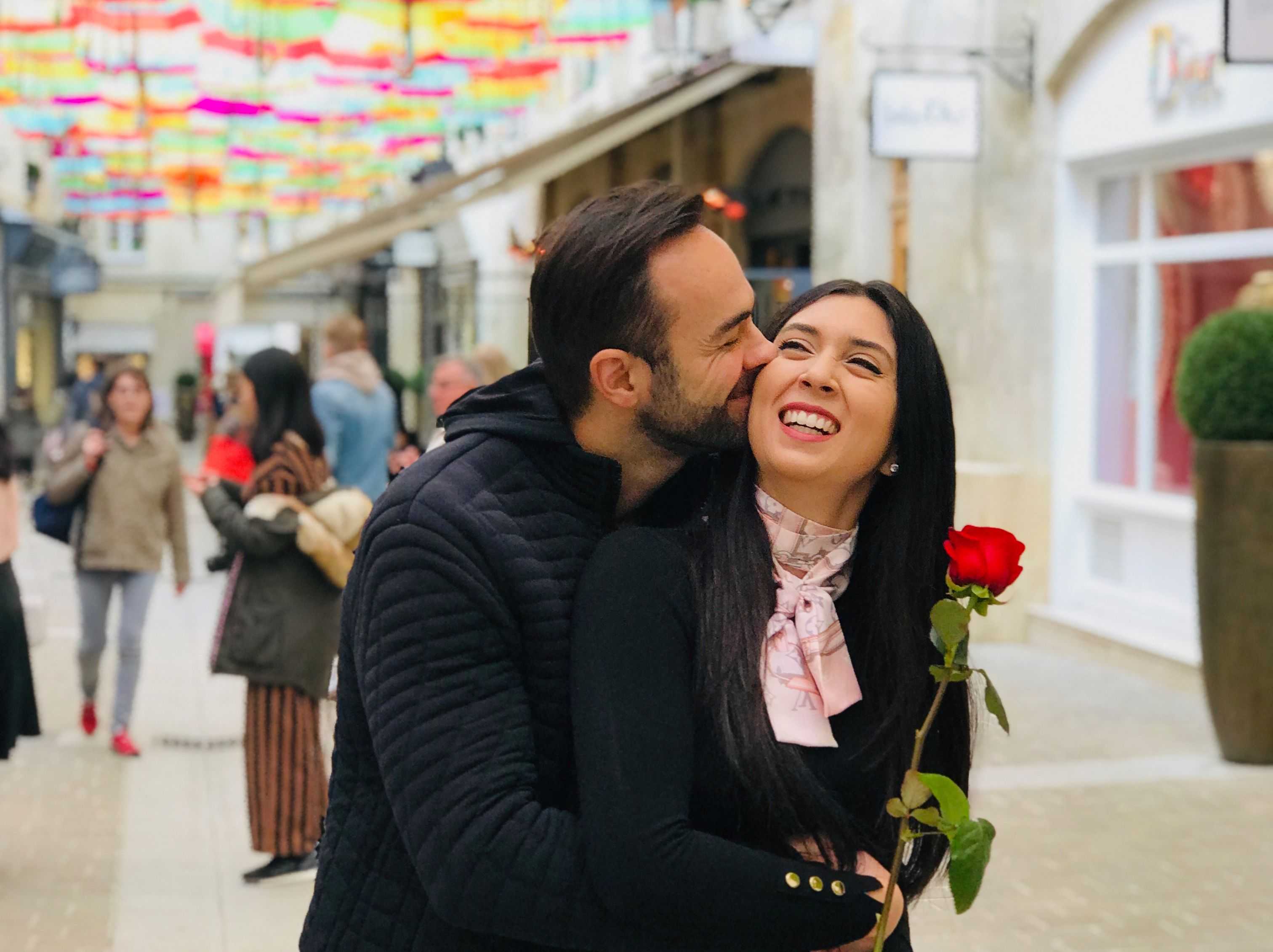 Andrea d'Agostini kissing Nicole Tabs while she holds a rose on a colorful background